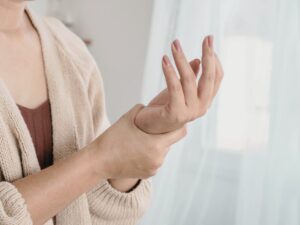 左手首を押さえて痛みを訴える女性。腱鞘炎や慢性的な肩こりに関連する左手首の不調をイメージした様子。