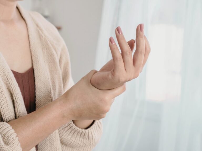 左手首を押さえて痛みを訴える女性。腱鞘炎や慢性的な肩こりに関連する左手首の不調をイメージした様子。