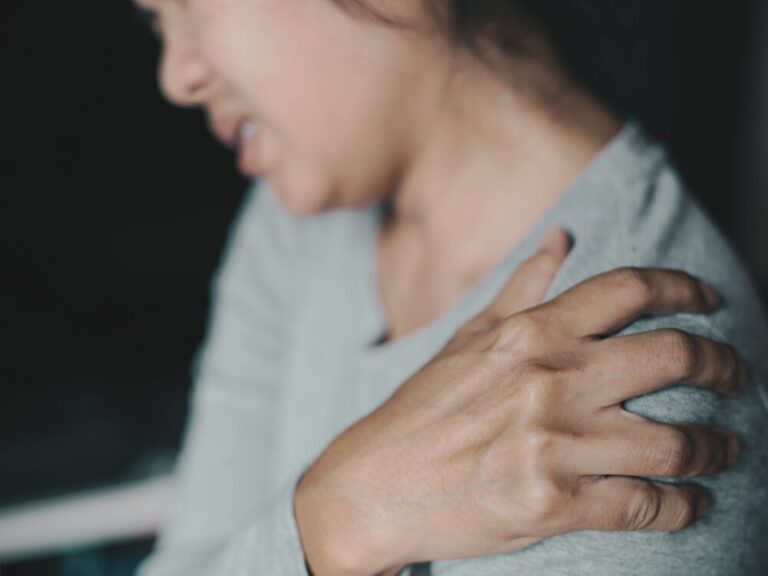 肩を押さえて痛みを訴える女性。長引く四十肩による不快感が見られる。