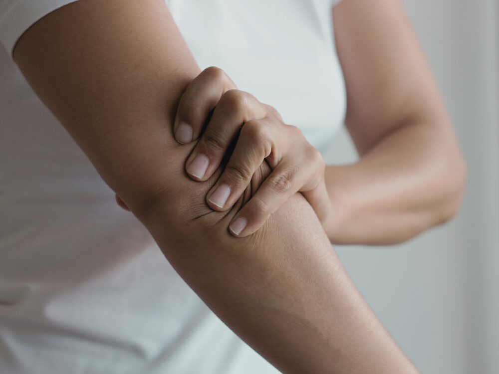 左手で右ひじを押さえている女性の上半身。腕やひじ周辺に痛みまたはしびれがある様子を示している。