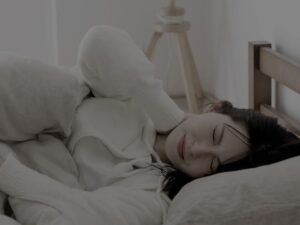 ベッドで横になりながら首の痛みに苦しむ女性。表情をゆがめ、首を押さえて眠れない様子を示している。