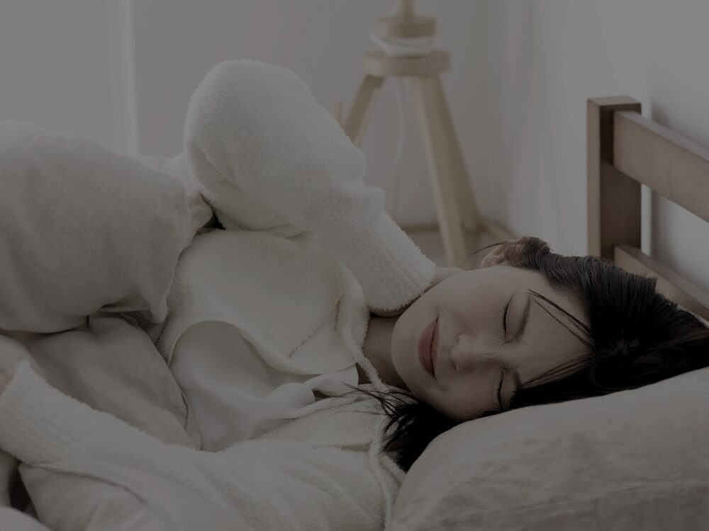 ベッドで横になりながら首の痛みに苦しむ女性。表情をゆがめ、首を押さえて眠れない様子を示している。