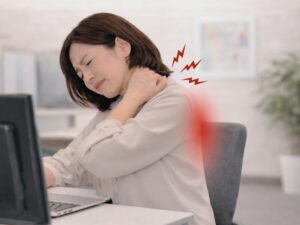 パソコン作業中に首から肩、背中の痛みを感じている40代女性。長時間のデスクワークにより慢性的な肩こりと背中の重だるさに悩んでいる様子。